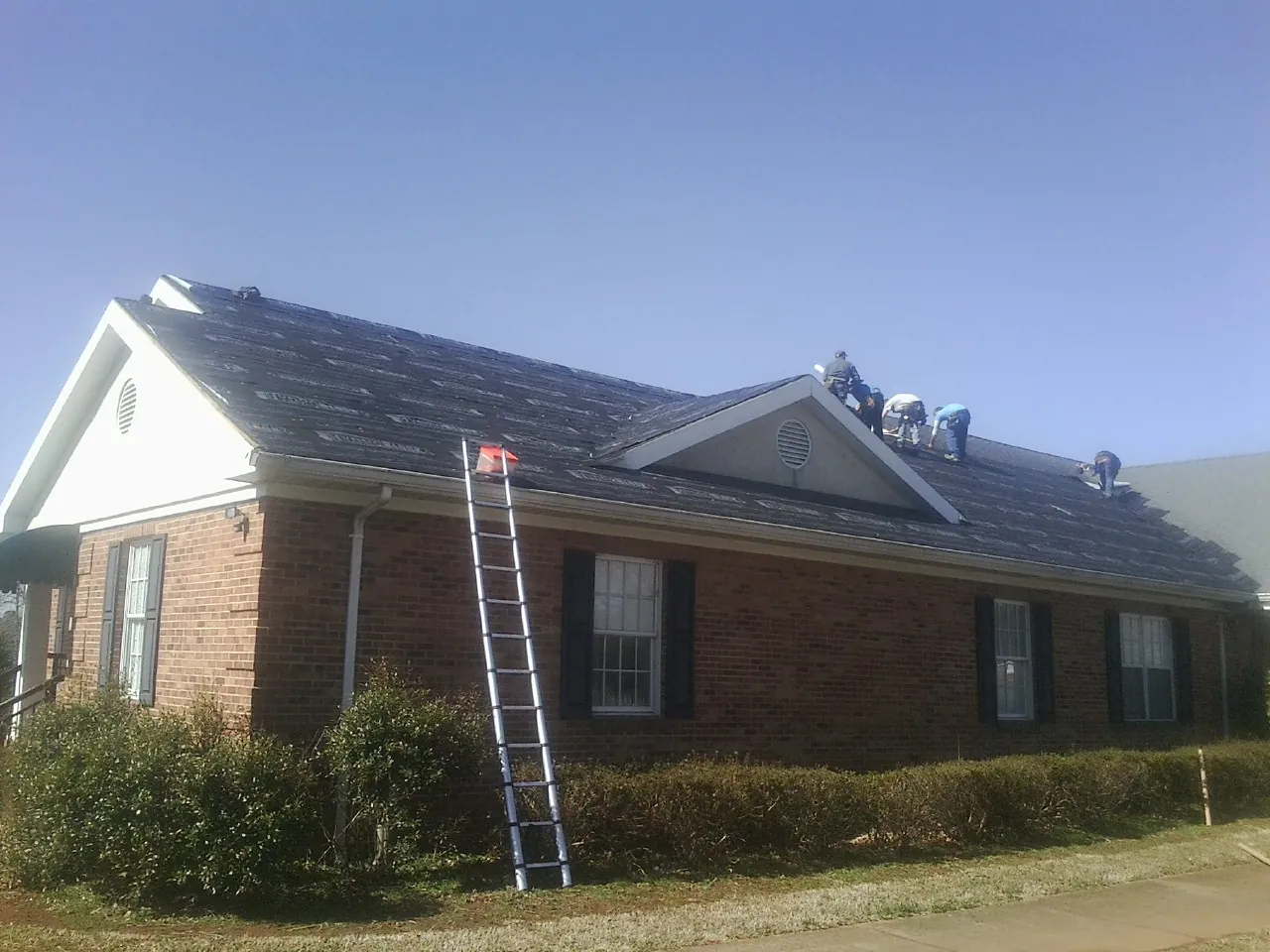 Crew tearing shingles off a brick ranch roof with a ladder set — Metal Roof Repair work by our crew in Keystone Heights