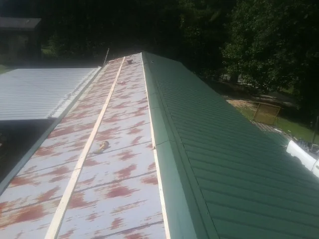 Old rusted panels beside newly installed green metal roofing — Wind Damage Roof Repair by Roofing Brothers in Keystone Heights