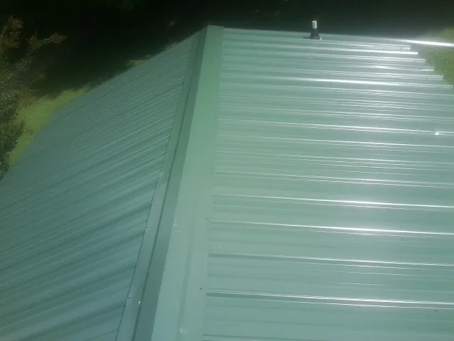 New green metal panels meeting at the ridge of a roof — Flat Roof Repair work by our crew in Keystone Heights